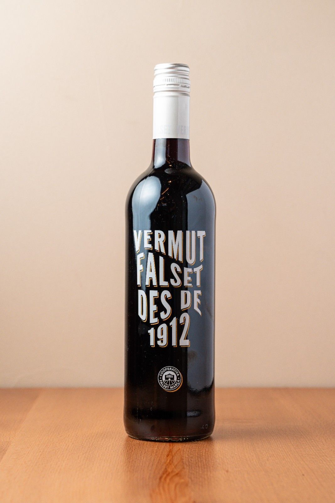 Botella de Vermut Falset Des de 1912 sobre una mesa de madera con fondo beige.
