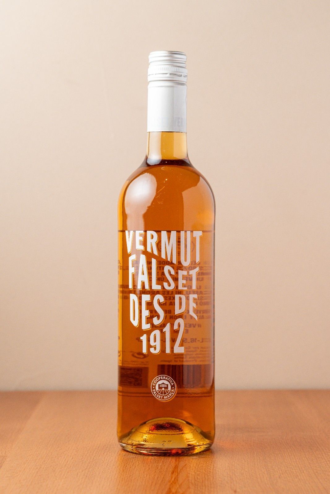 Botella de vermut ámbar sobre una superficie de madera con una etiqueta blanca que dice “Vermut Falset des Priorat 1912”.