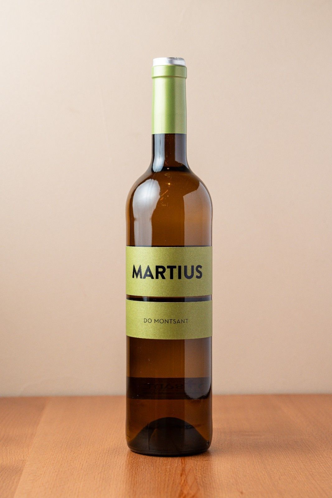 Botella de vino marrón con tapón verde y etiqueta MARTIUS colocada sobre una superficie de madera.