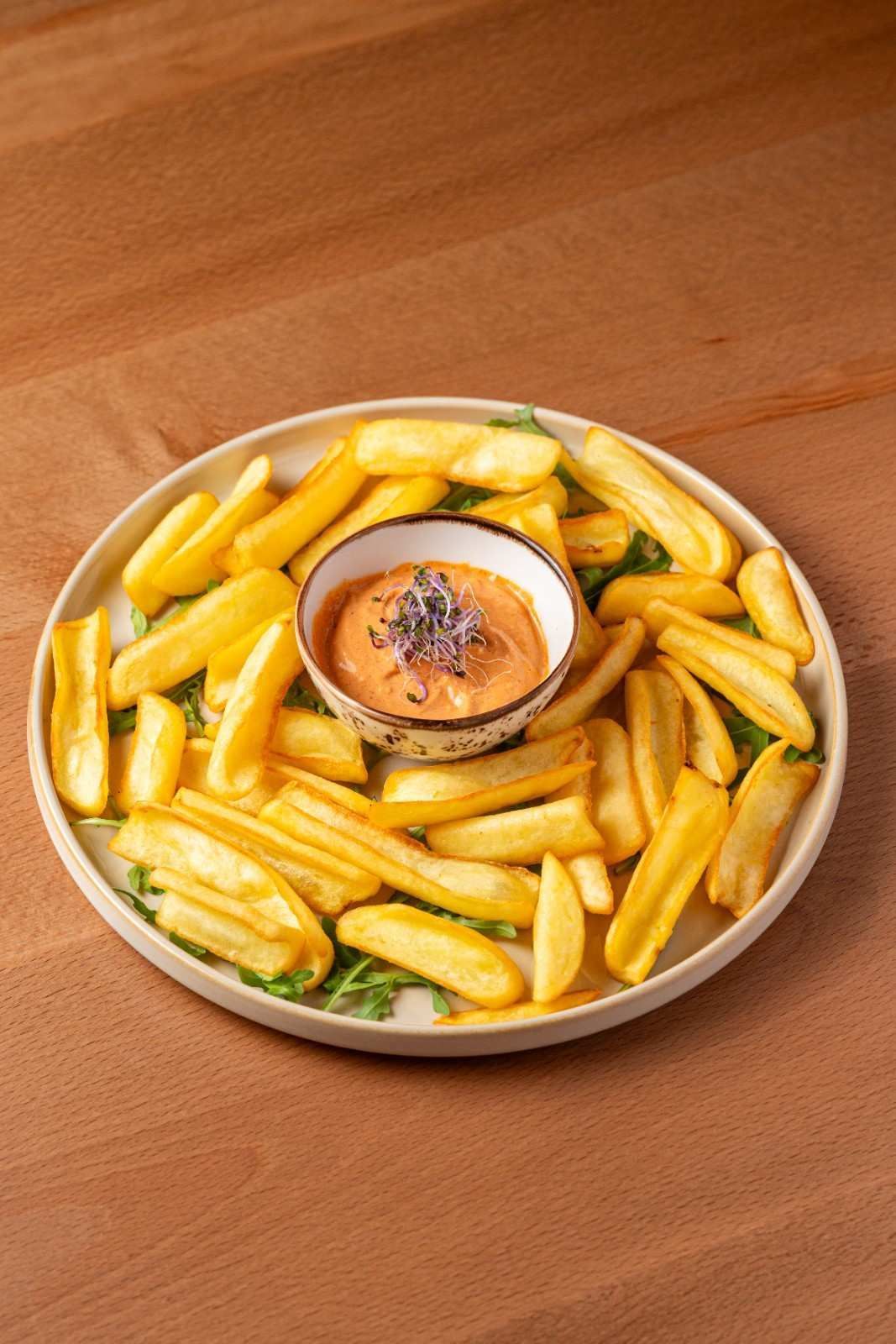 Papas fritas amarillas alrededor de un tazón para salsa en el centro sobre un plato encima de una mesa de madera.