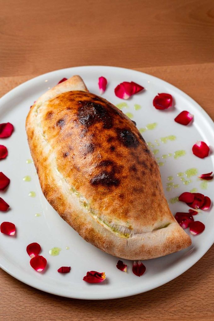 Pastel relleno horneado sobre un plato blanco, adornado con semillas de granada sobre una mesa de madera.