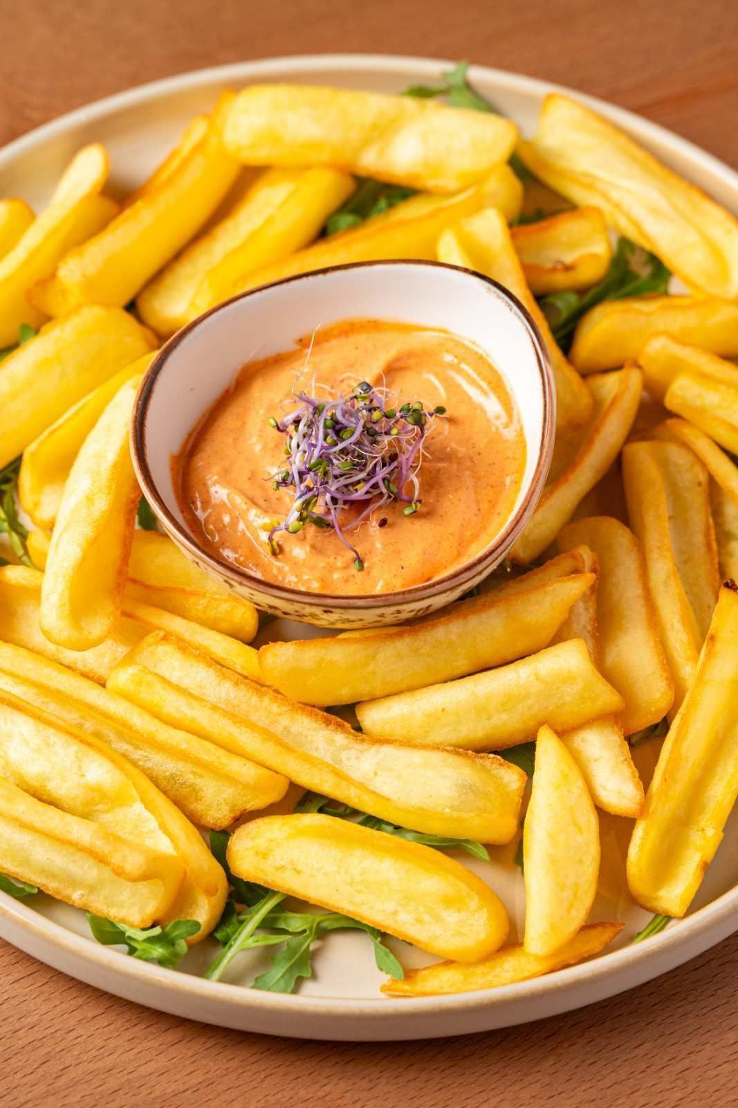 Plato de patatas fritas gruesas con un pequeño cuenco de salsa de naranja para mojar, aderezado con hierbas.