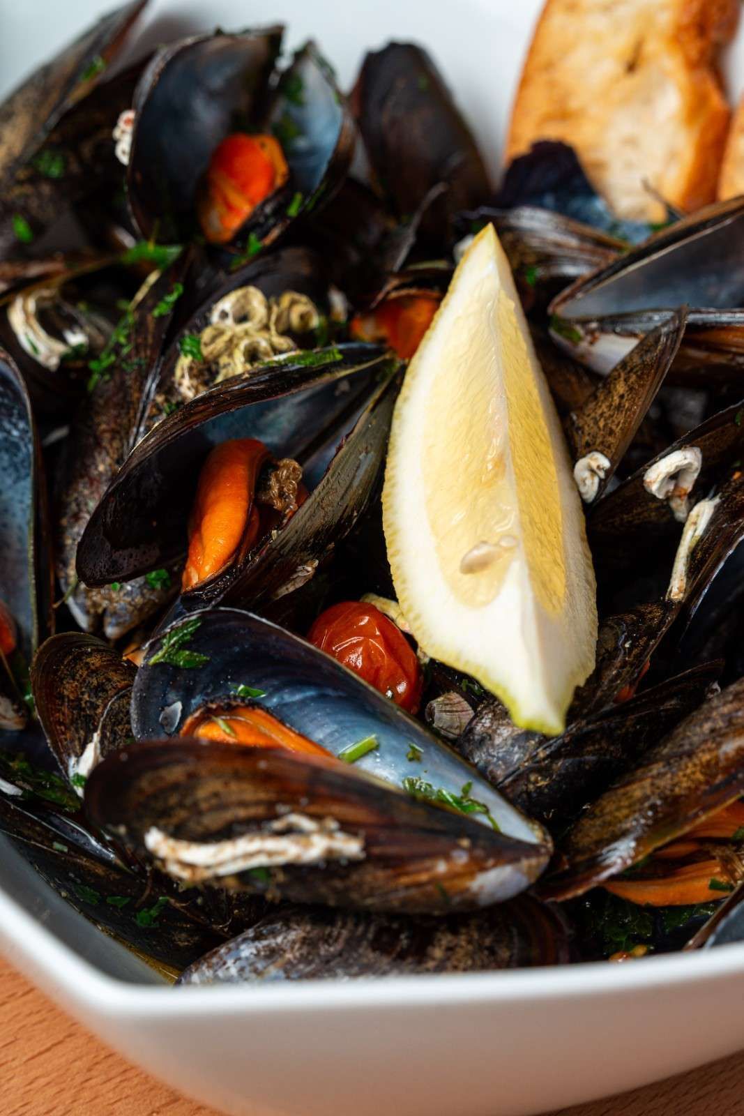 Bol de mejillones en caldo con una rodaja de limón y hierbas.