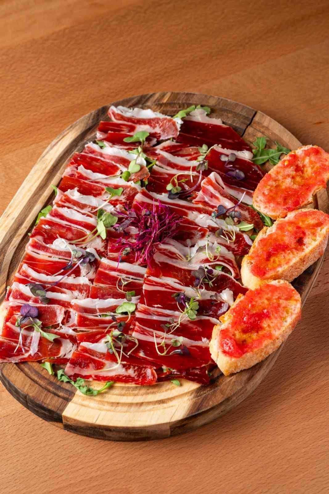 Prosciutto en lonchas sobre una tabla de madera con higos y verduras sobre una mesa.