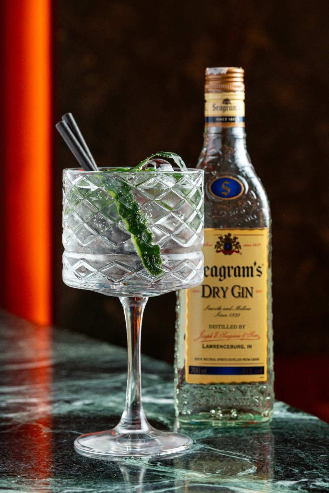 Un martini de ginebra con menta y una botella de ginebra Tanqueray Dry sobre una barra de mármol.