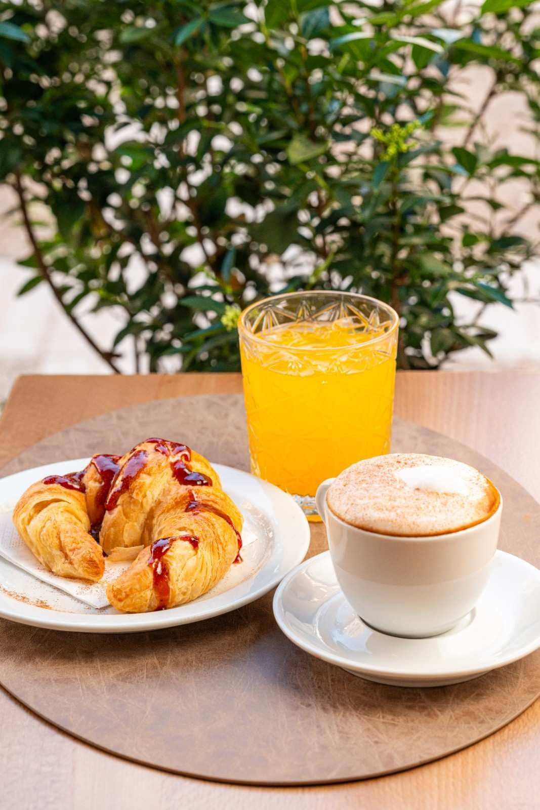 Pastel, zumo de naranja y capuchino sobre una mesa con un fondo de hojas.