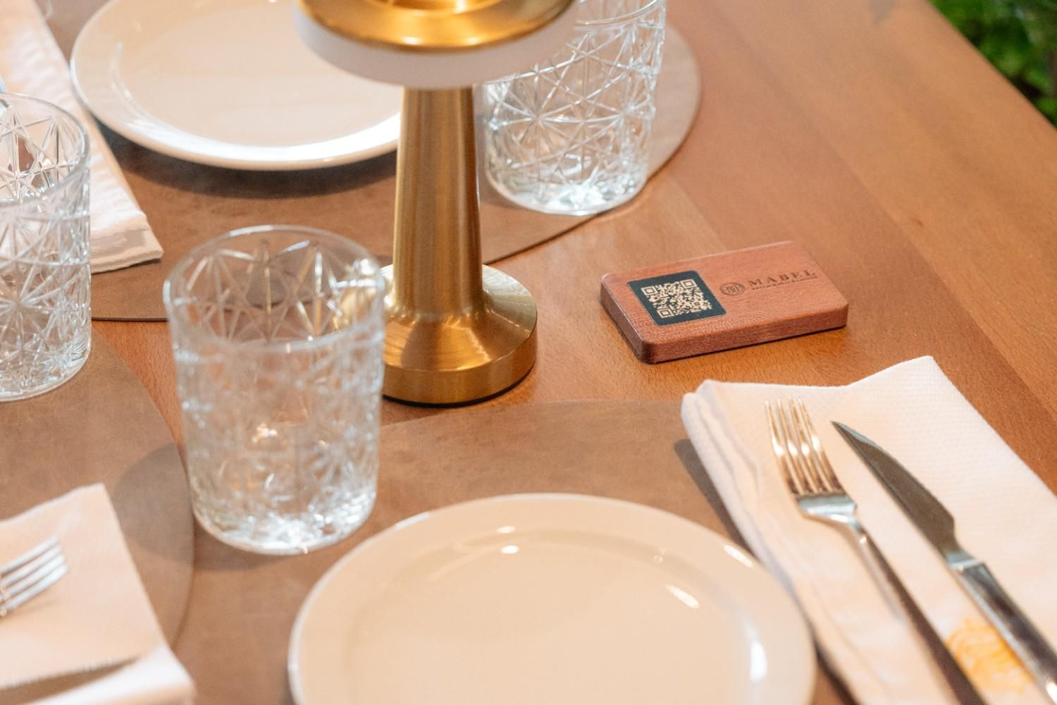 Coloca la mesa del comedor con platos, vasos, cubiertos y un candelabro dorado sobre una superficie de madera.