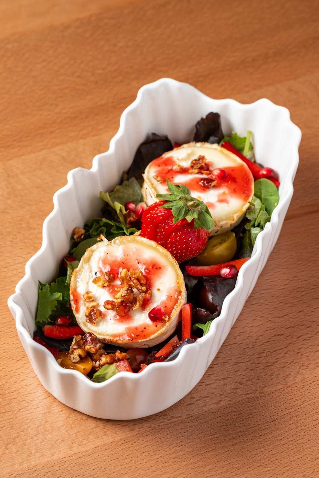 Plato de vieiras blancas con una ensalada colorida coronada con dos huevos escalfados sobre una mesa de madera.