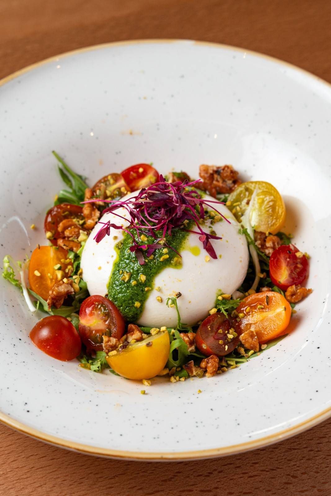Burrata en un plato blanco con tomates cherry, hierbas y un chorrito de aceite de oliva.