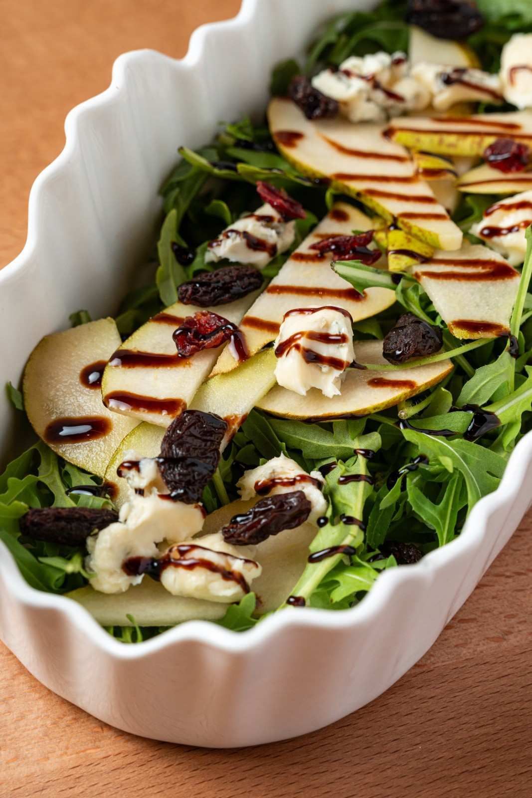 Ensalada de rúcula con rodajas de pera y un chorrito de vinagre balsámico en un plato blanco con vieiras.