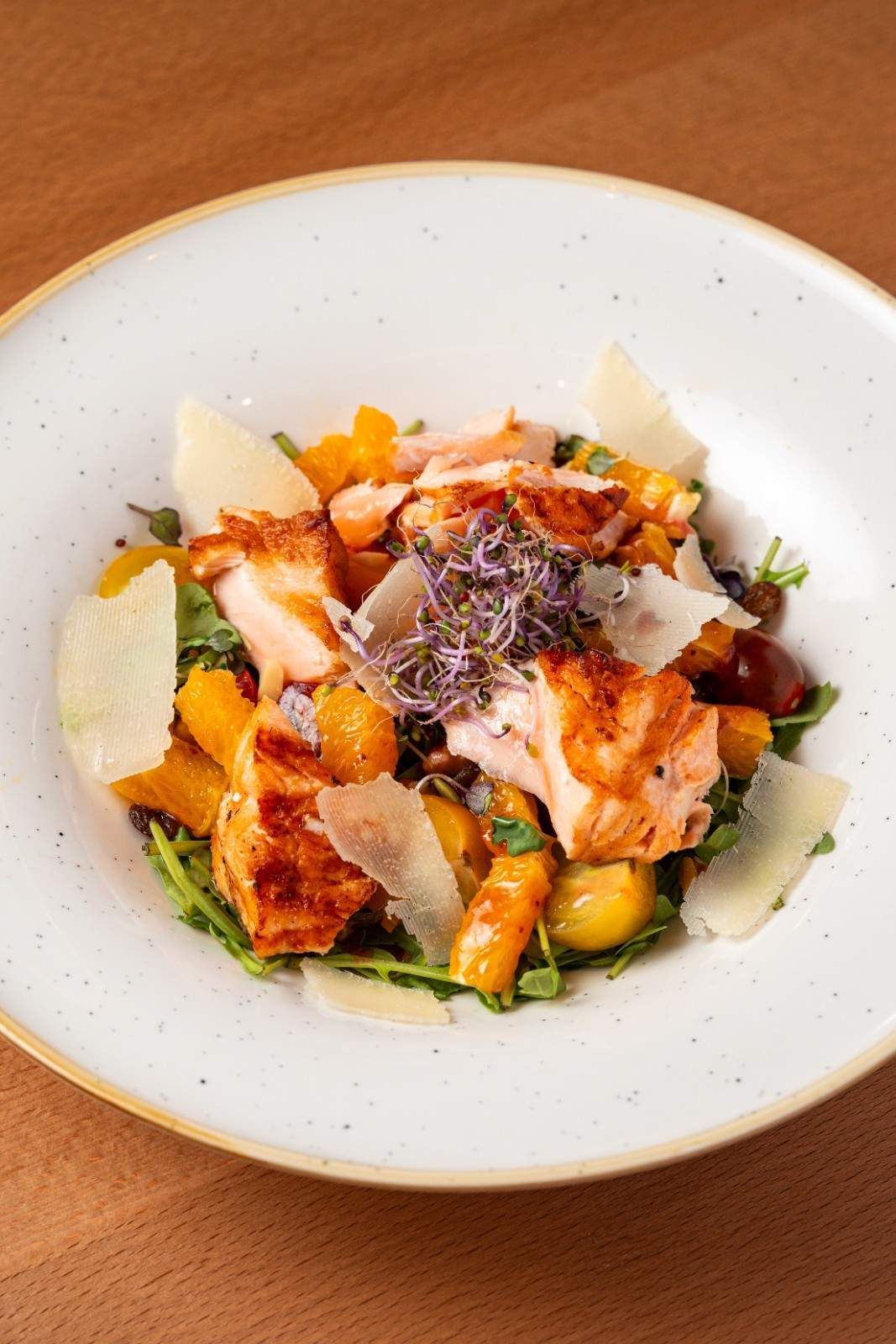Ensalada con verduras mixtas, queso rallado y aderezo en un plato blanco sobre una mesa de madera.