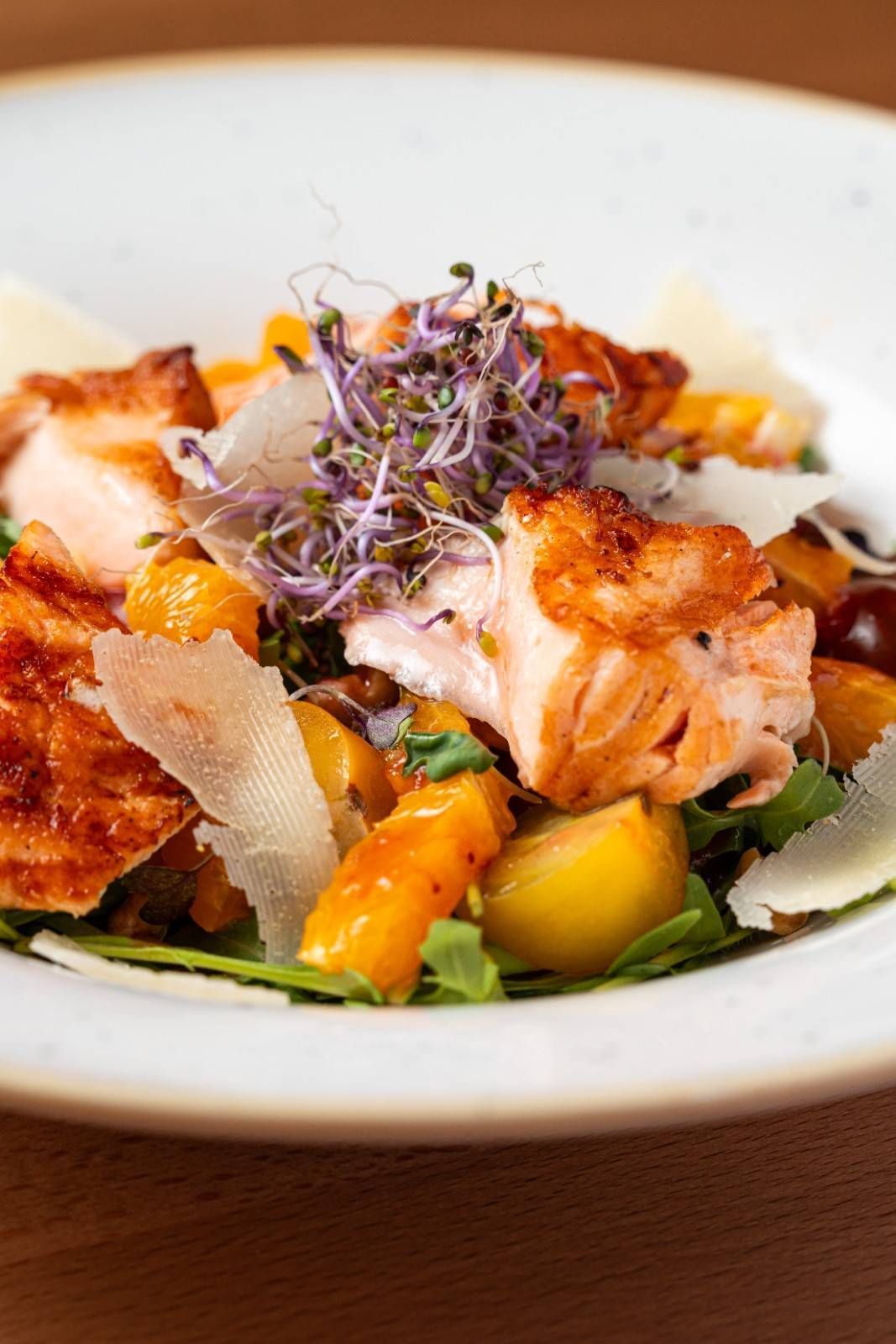 Ensalada de salmón a la parrilla con rodajas de naranja y brotes tiernos en un plato blanco.