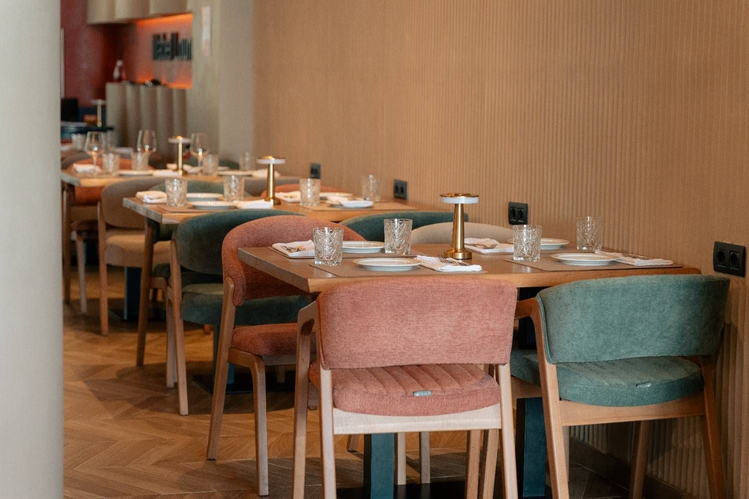Elegante comedor de restaurante con mesas puestas, sillas rosas y verdes y cálidas paredes revestidas de madera.