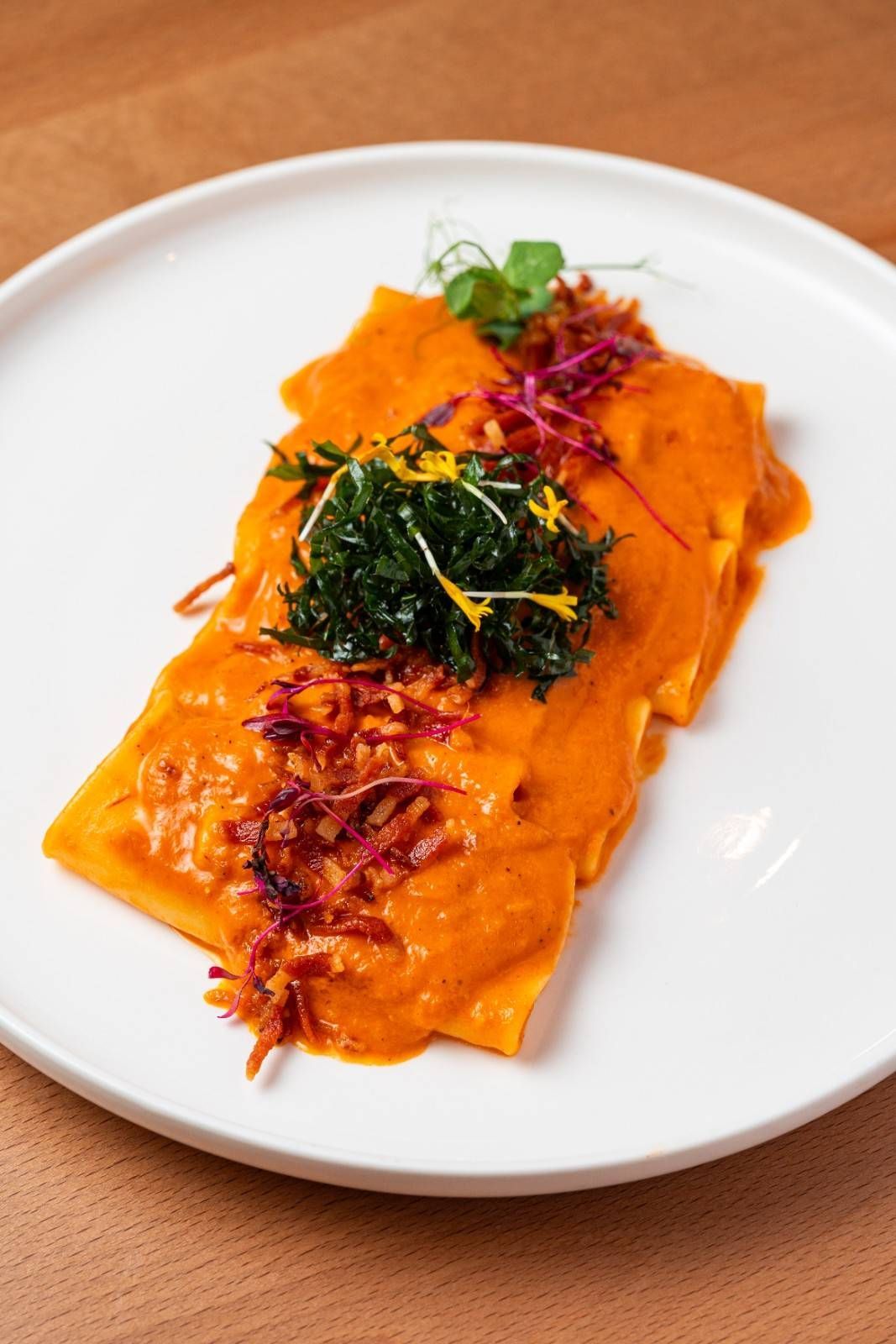 Pasta rellena con salsa de naranja servida en un plato blanco, decorada con hierbas y guarnición roja.