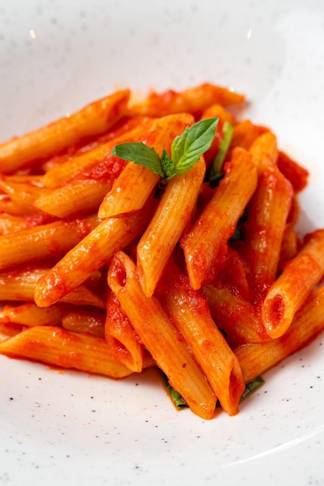 Pasta penne en salsa de tomate rojo cubierta con albahaca fresca en un plato blanco.