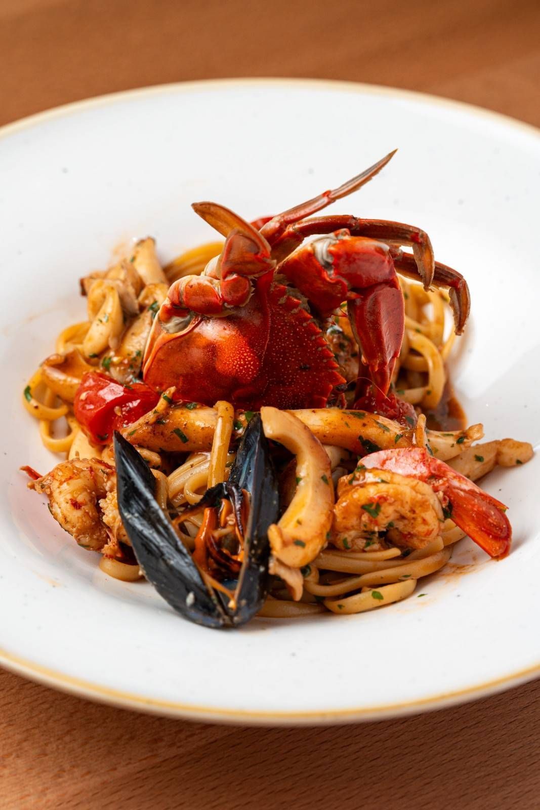 Pasta con mariscos (cangrejo, camarones y mejillones) en un tazón blanco sobre una mesa.