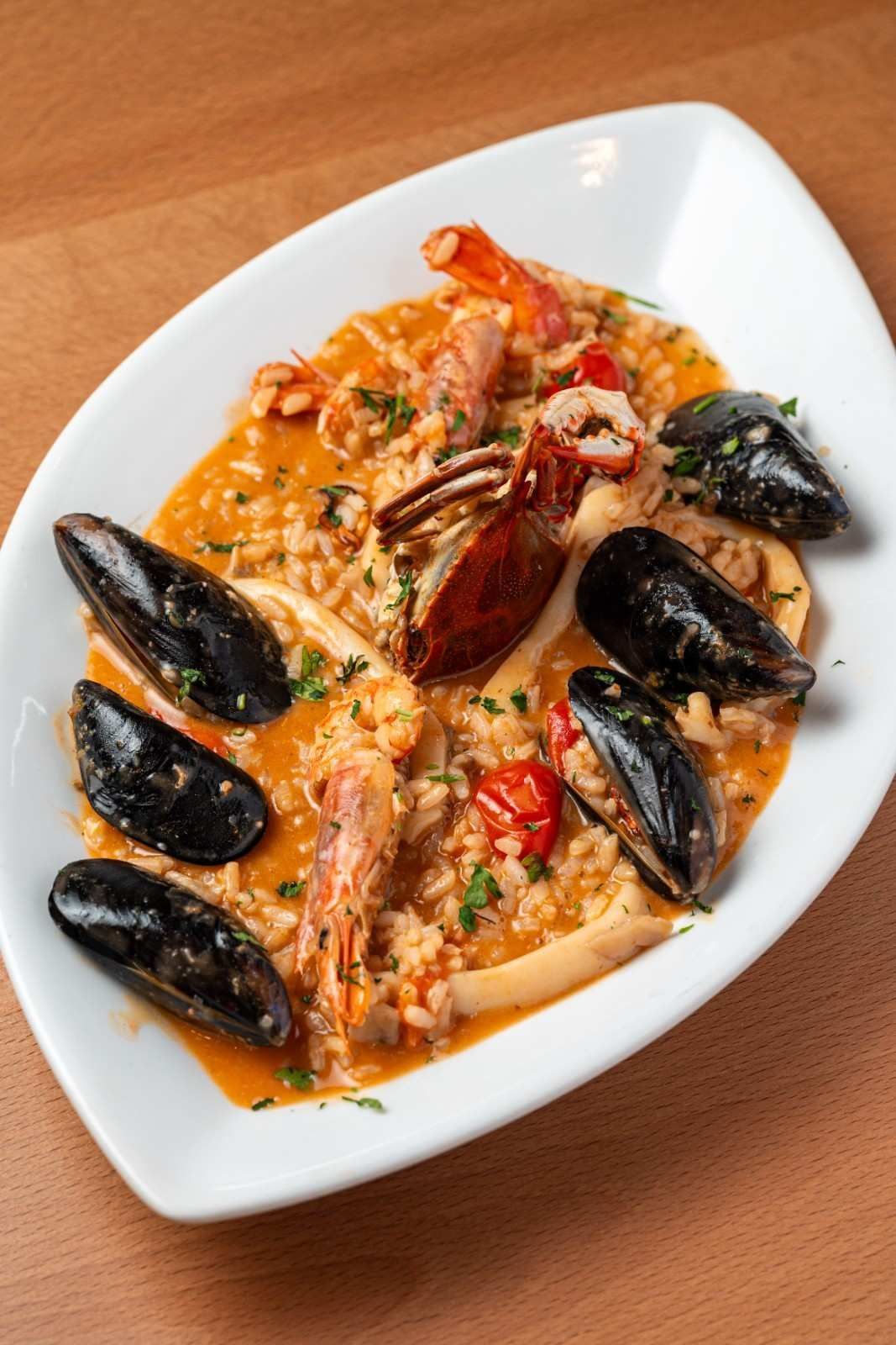 Risotto de marisco con mejillones y langosta en un plato rectangular blanco.
