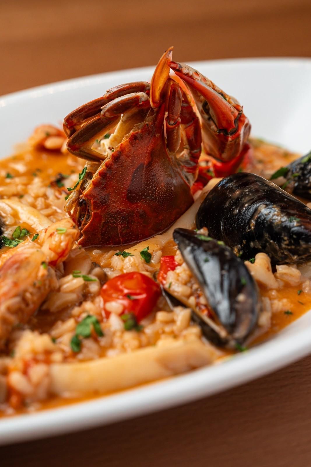 Pasta con mariscos, gambas y mejillones en salsa roja sobre un plato blanco.