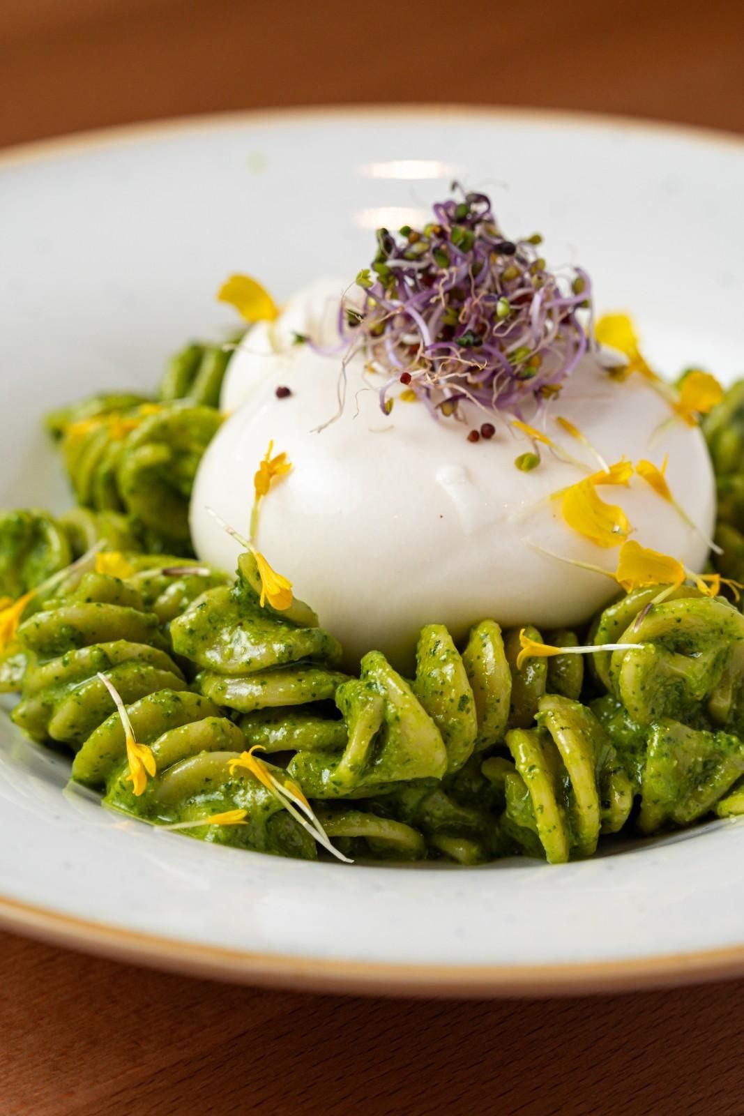 Fusilli con pesto verde, coronado con un huevo escalfado y microvegetales en un plato blanco.