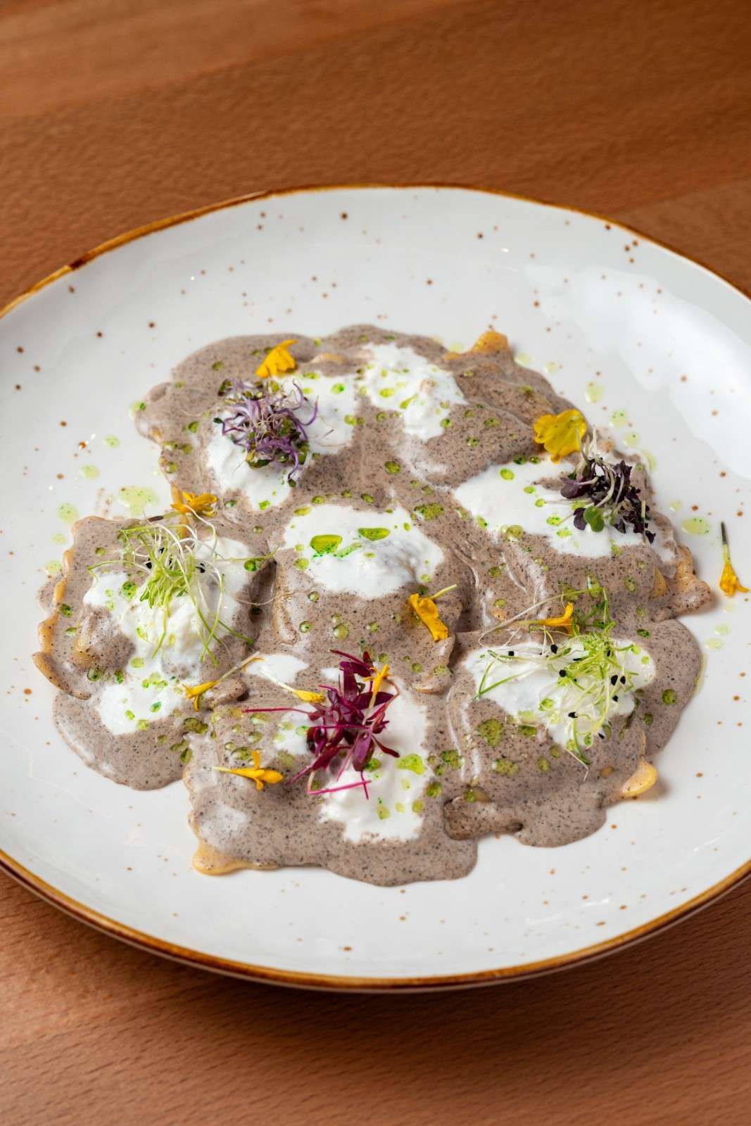 Raviolis cremosos de champiñones adornados con hierbas y flores comestibles en un plato blanco.