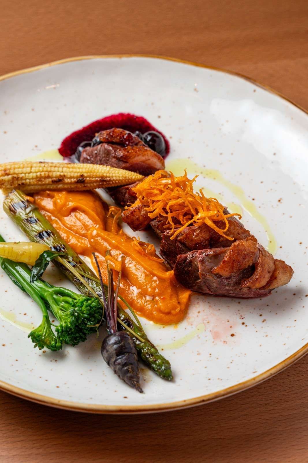 Pollo asado gourmet emplatado con verduras y salsa de frutos rojos en un plato blanco.