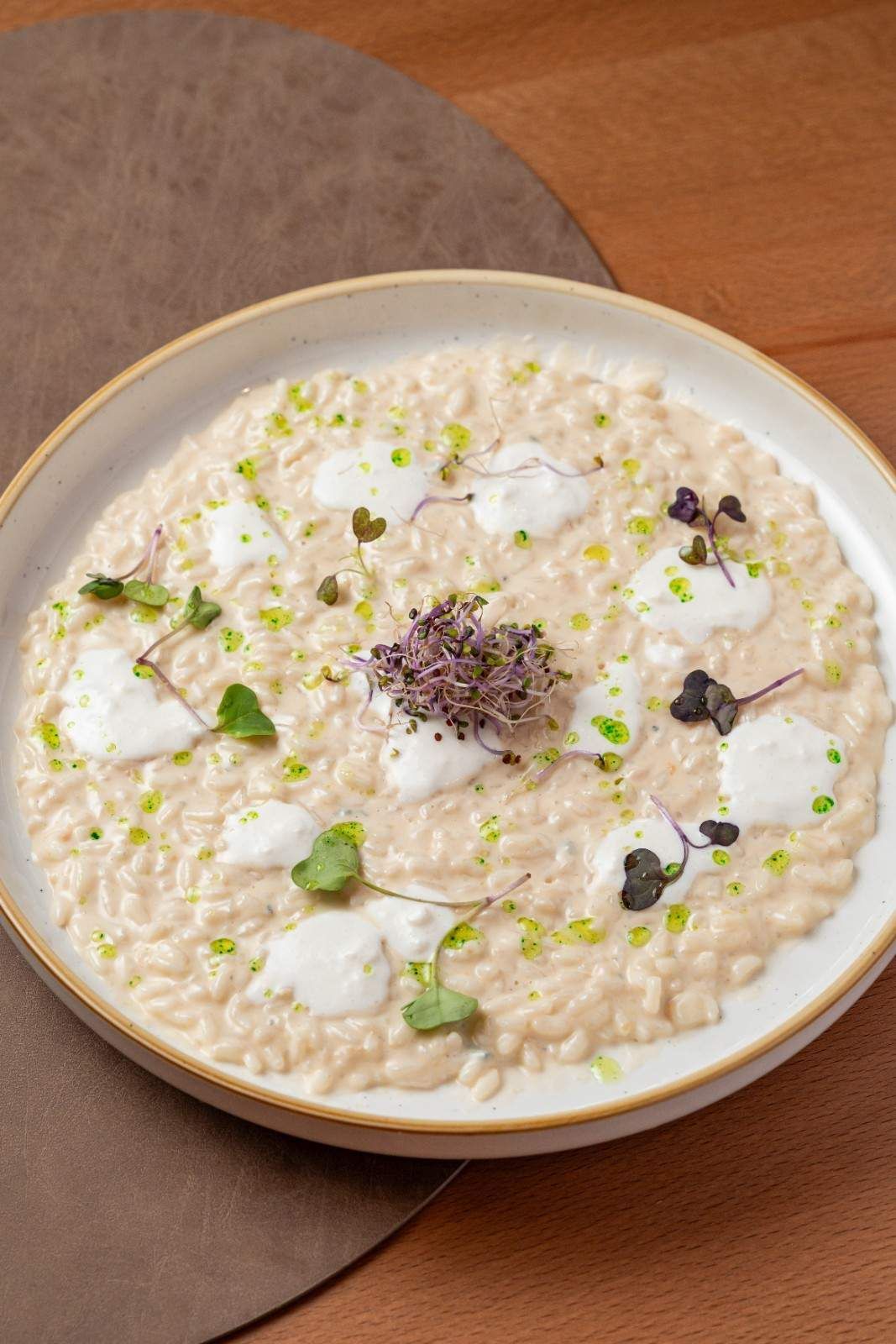 Un bol de risotto cremoso con hierbas y brotes sobre una mesa de madera.