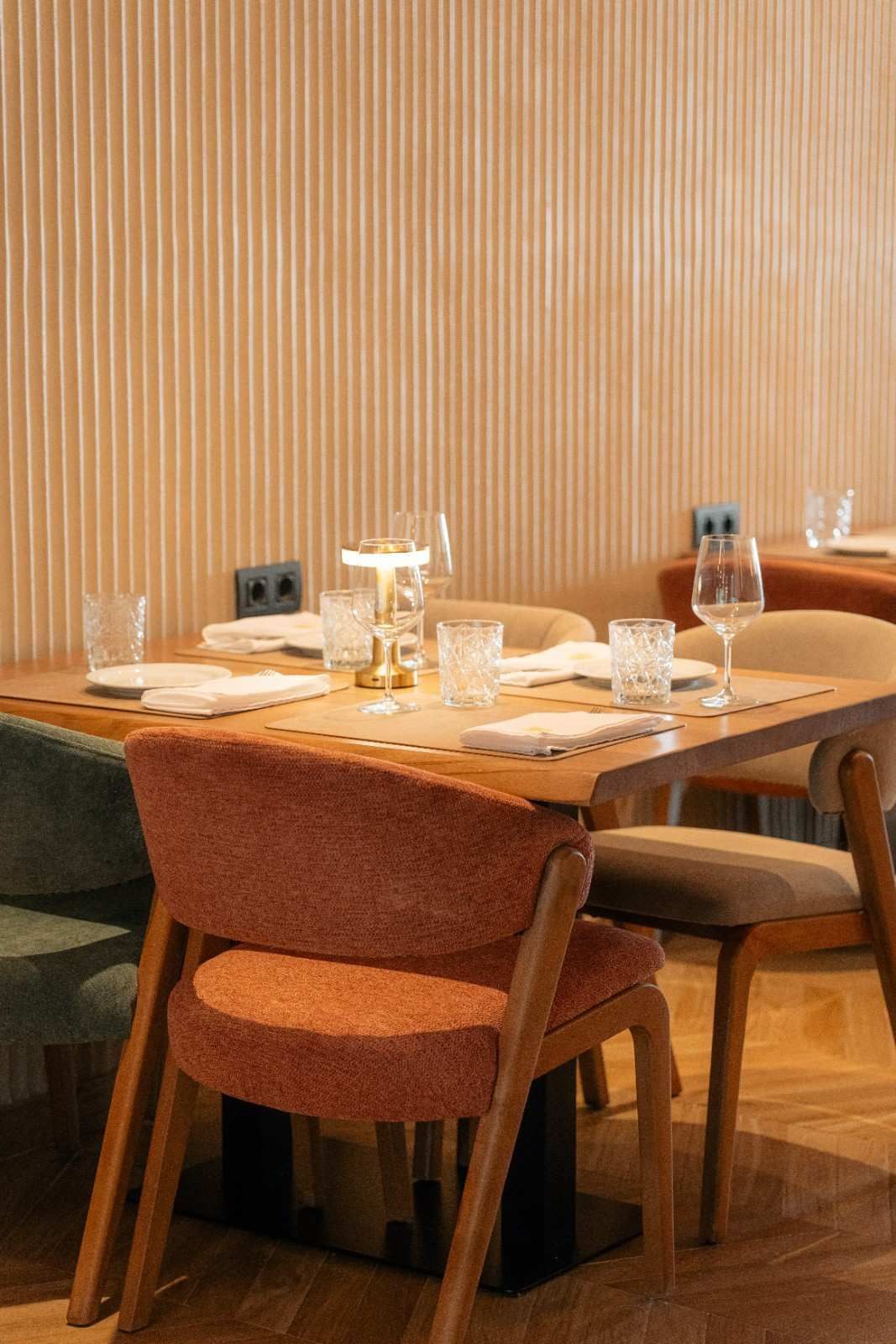 Una acogedora mesa de restaurante con sillas de madera, copas de vino, velas y platos cuidadosamente dispuestos.