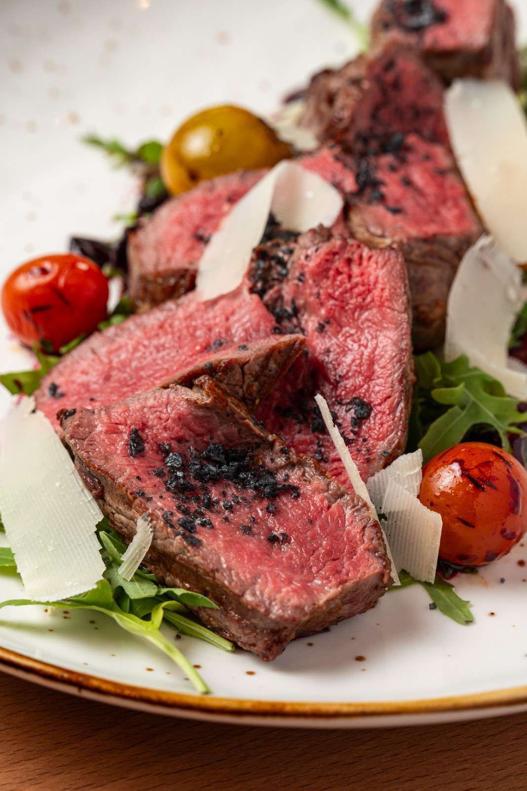 Filete rosado sellado con tomates cherry y verduras en un plato blanco, cubierto con queso rallado.