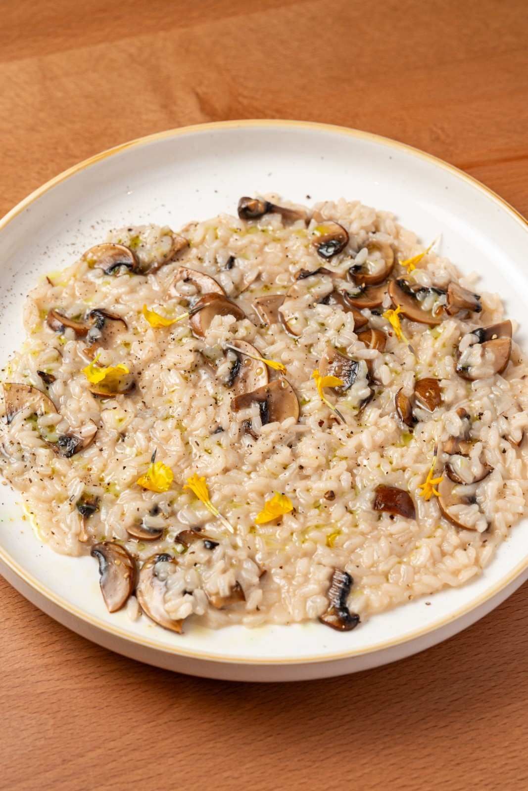 Plato de arroz cremoso con champiñones y maíz sobre una mesa de madera.
