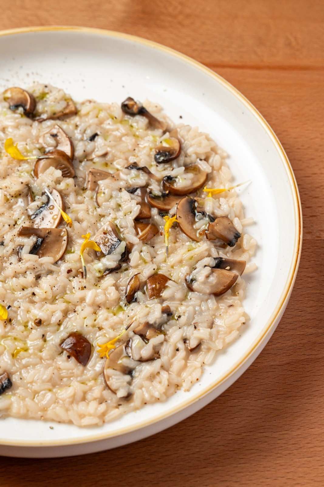 Risotto de champiñones en un plato blanco sobre una mesa de madera.