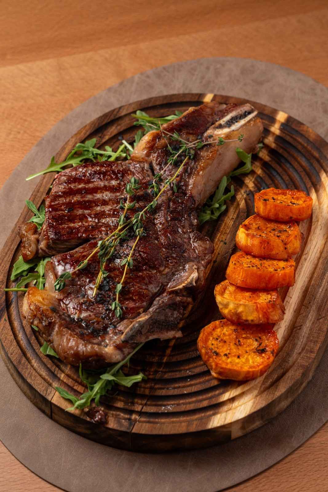 Filete a la parrilla con hierbas y patatas gajo asadas sobre una tabla de madera.