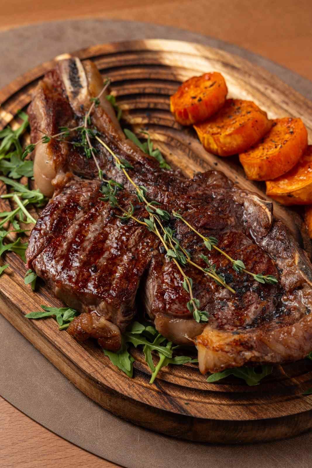 Filete a la parrilla con romero sobre una tabla de madera, servido con patatas gajo asadas.