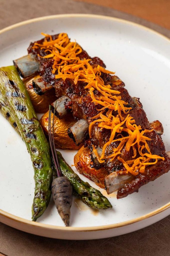 Filete a la parrilla con espárragos asados y guarnición de naranja rallada en un plato blanco.