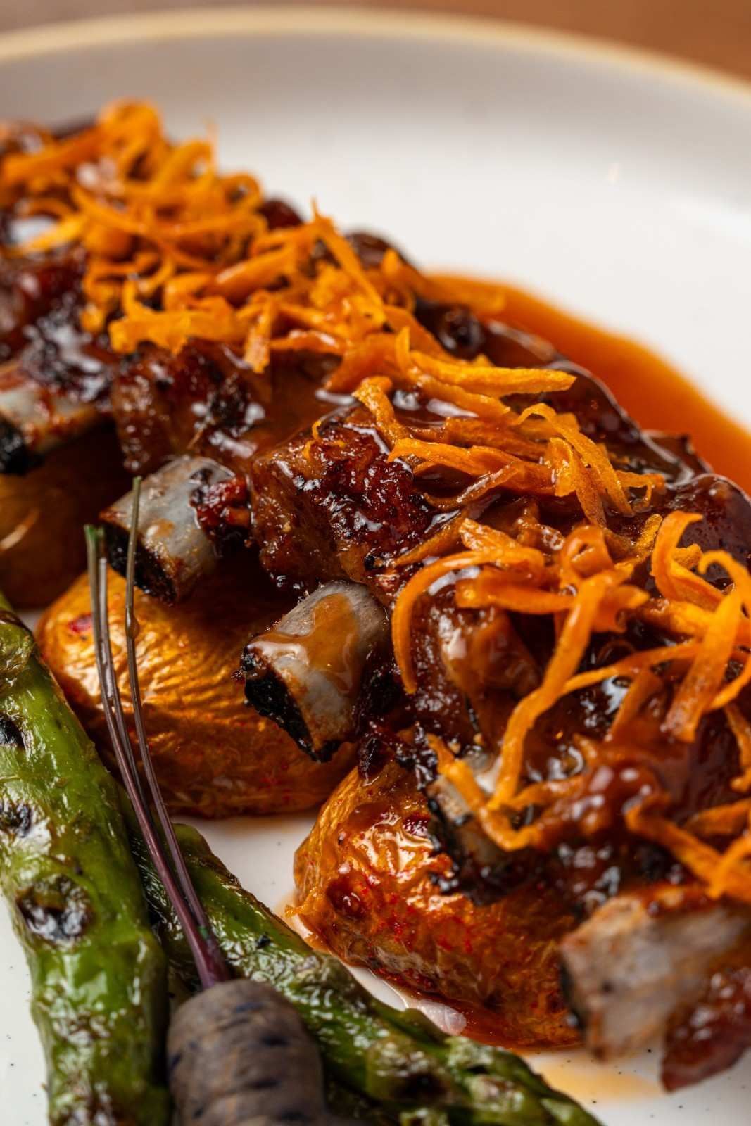 Primer plano de carne glaseada adornada con zanahorias ralladas y judías verdes en un plato blanco.