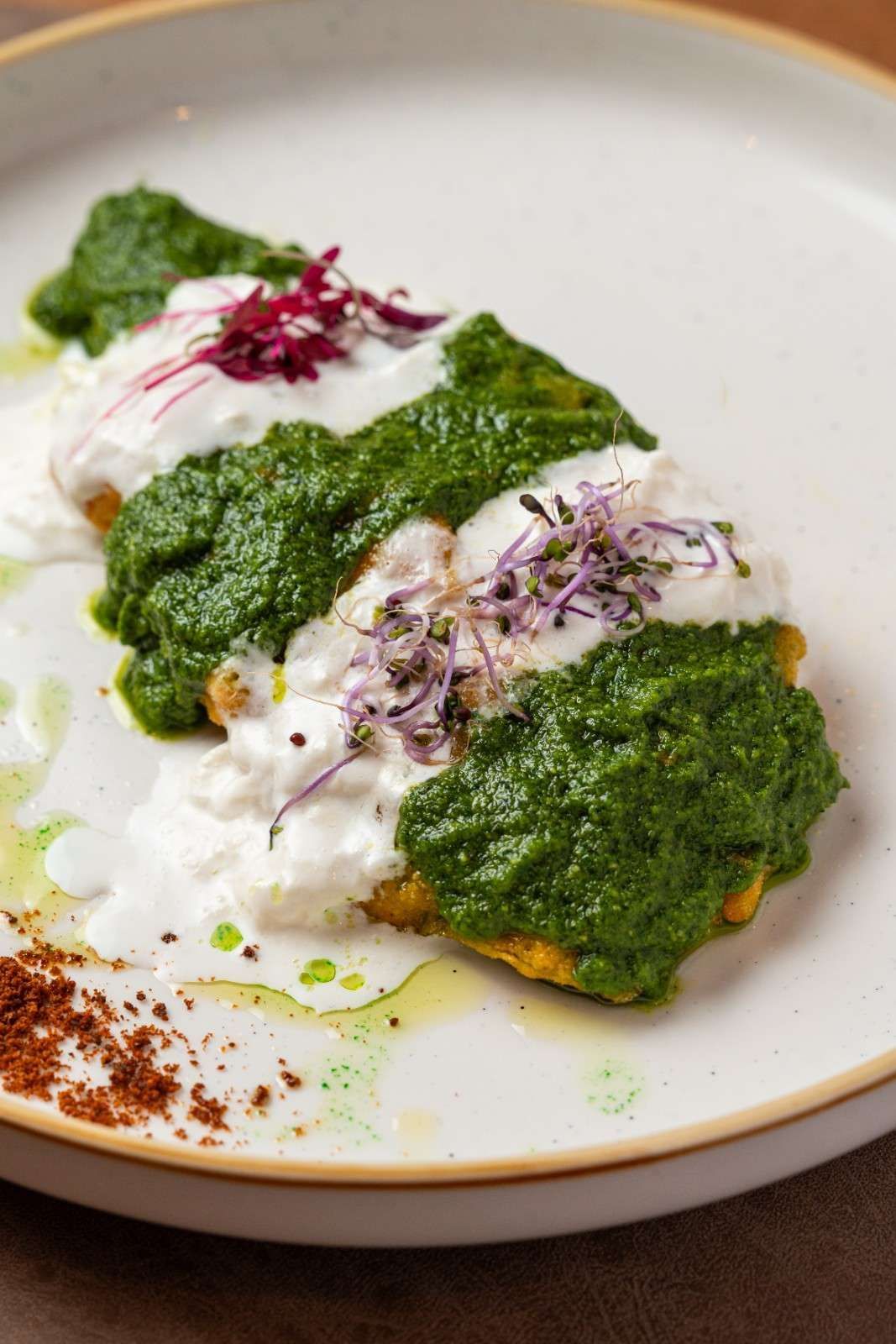 Bocados salados con cobertura verde, salsa blanca y hierbas, servidos en un plato blanco.
