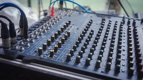Primer plano de una mesa de mezclas de sonido con varias perillas y conectores de entrada; predomina un esquema de colores azul y negro.