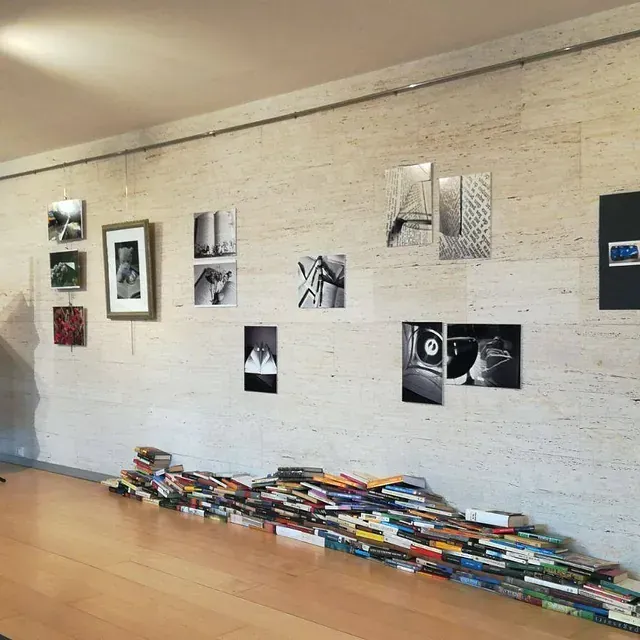 Una pared de galería de arte exhibe fotos en blanco y negro. Una pila de libros reposa en el suelo, debajo de las obras de arte.