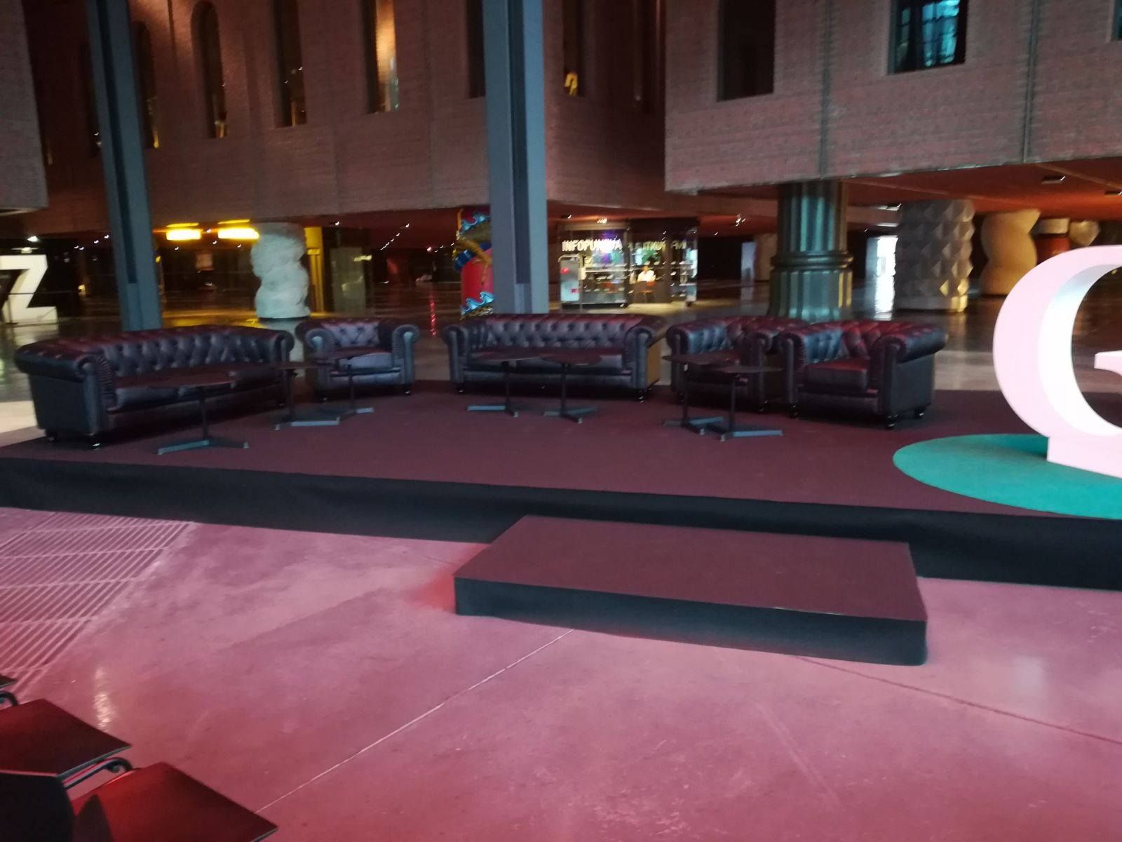 Un escenario con sofás de cuero y mesas pequeñas en un auditorio. Una gran "G" de Google está a la derecha.