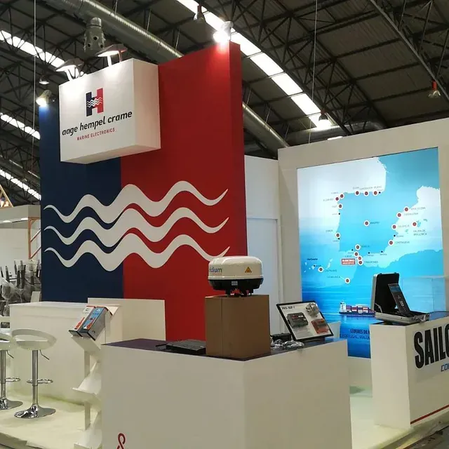Stand de Auge Bernel Crane en una feria comercial, con su logotipo, un mapa y equipo de exhibición. Combinación de colores blanco, azul y rojo.