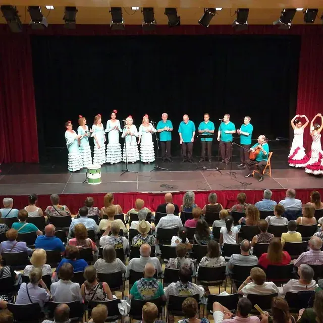 Un coro y un guitarrista actúan en un escenario con dos bailaoras de flamenco y un público sentado en un auditorio.