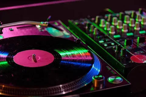 Primer plano de una configuración de DJ con un disco de vinilo en un tocadiscos, iluminado con luces neón de color rosa y verde.