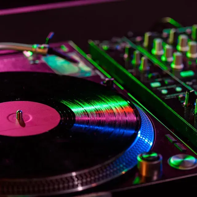 Tocadiscos con un disco de vinilo iluminado con neón verde, rosa y azul, al lado de una mesa de mezclas para DJ.
