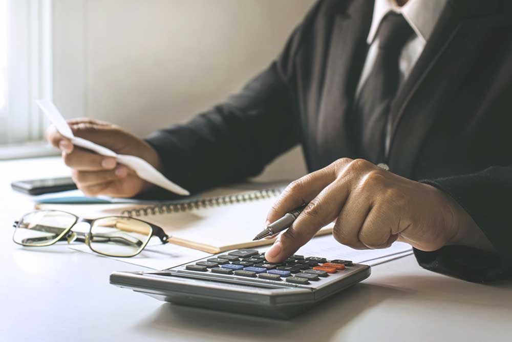 Un hombre con traje y corbata usa una calculadora mientras sostiene un trozo de papel.