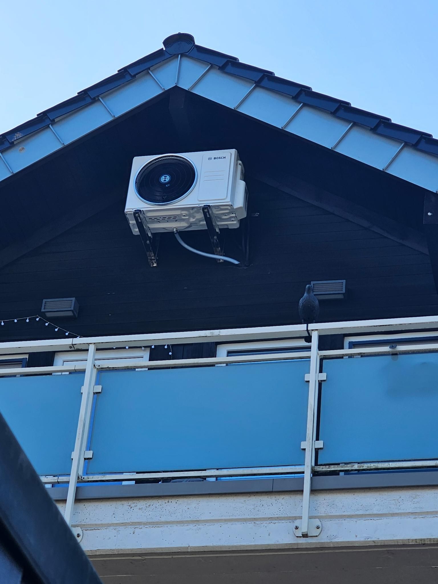 Blauer Hausgiebel mit einer über dem Balkongeländer montierten Außenklimaanlage