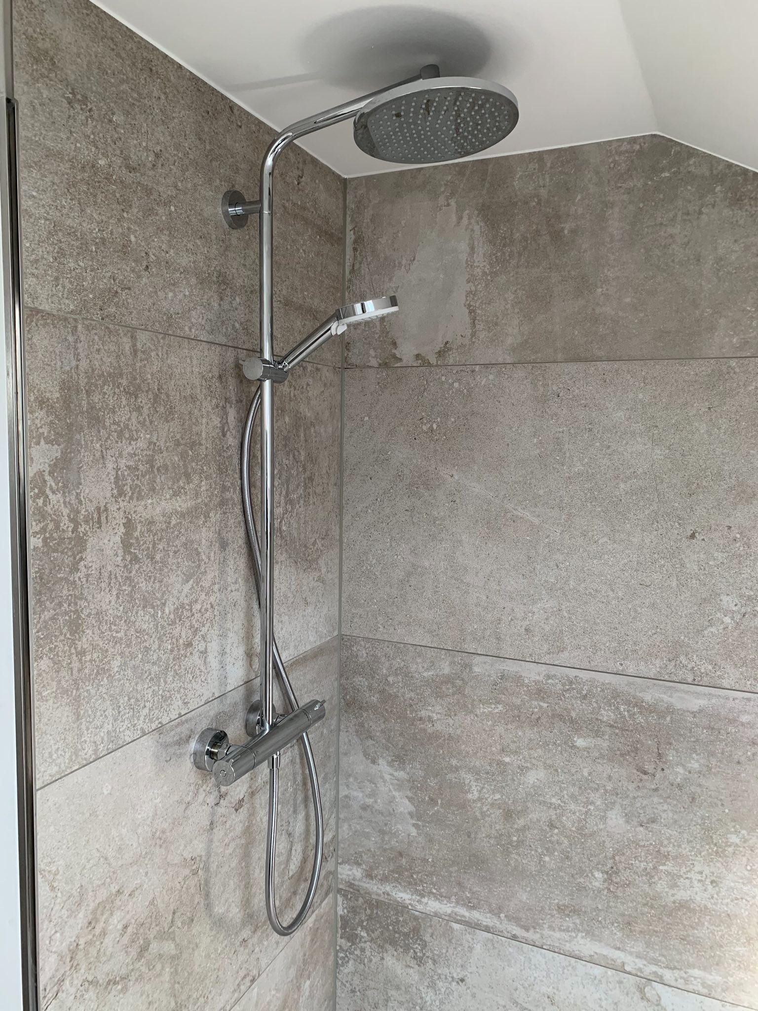 Moderne, ebenerdige Dusche mit Regenduschkopf und Handbrause an beigefarbenen Fliesenwänden