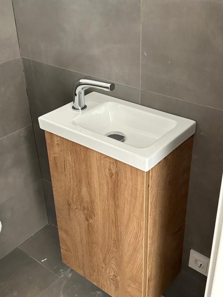 Kleines Badezimmerwaschbecken mit weißem Becken, verchromter Armatur und Holzschrank vor grau gefliesten Wänden