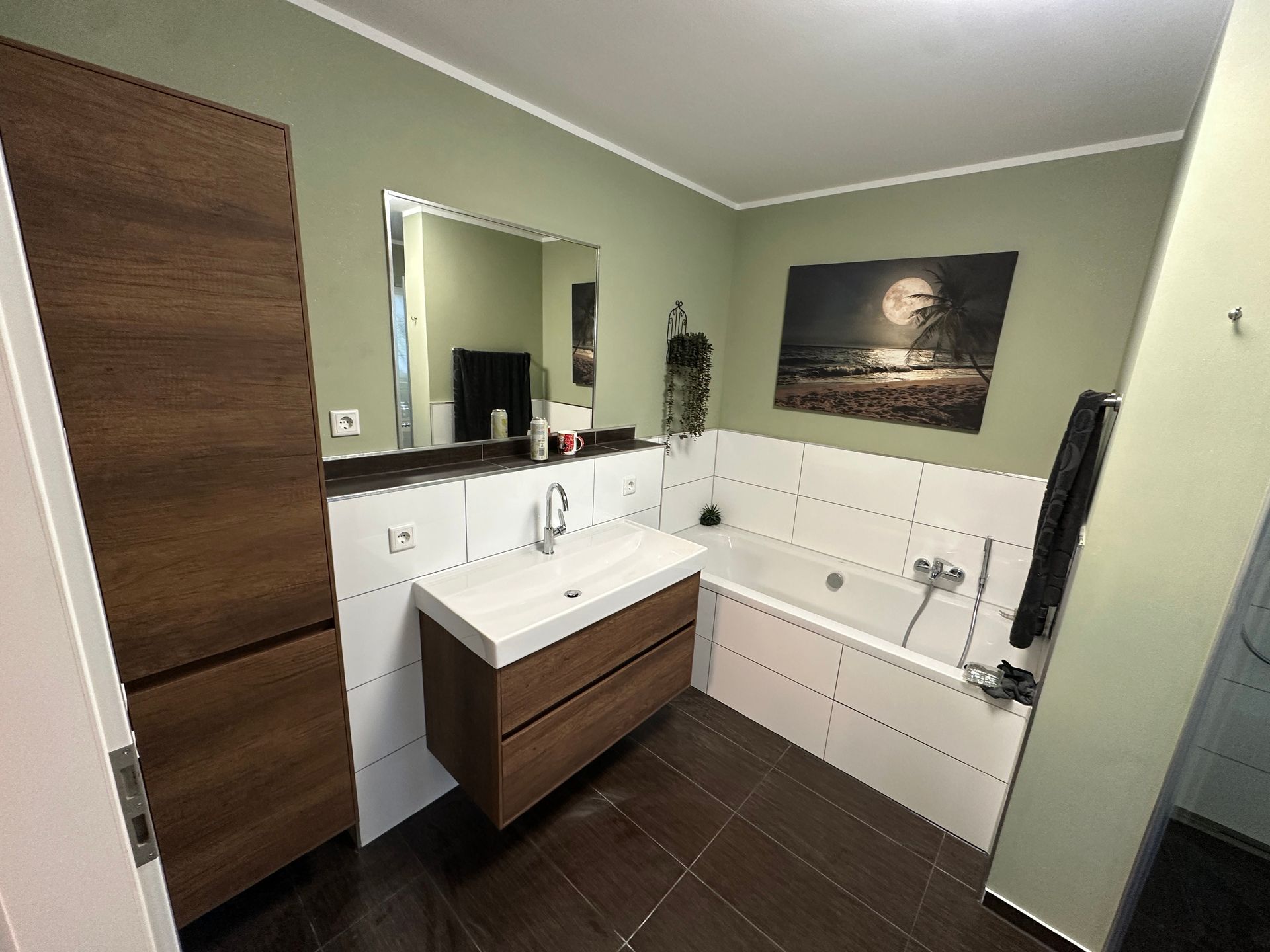 Modernes Badezimmer mit Waschtisch, großem Spiegel, weißen Fliesen, braunen Schränken und dunklen Bodenfliesen.