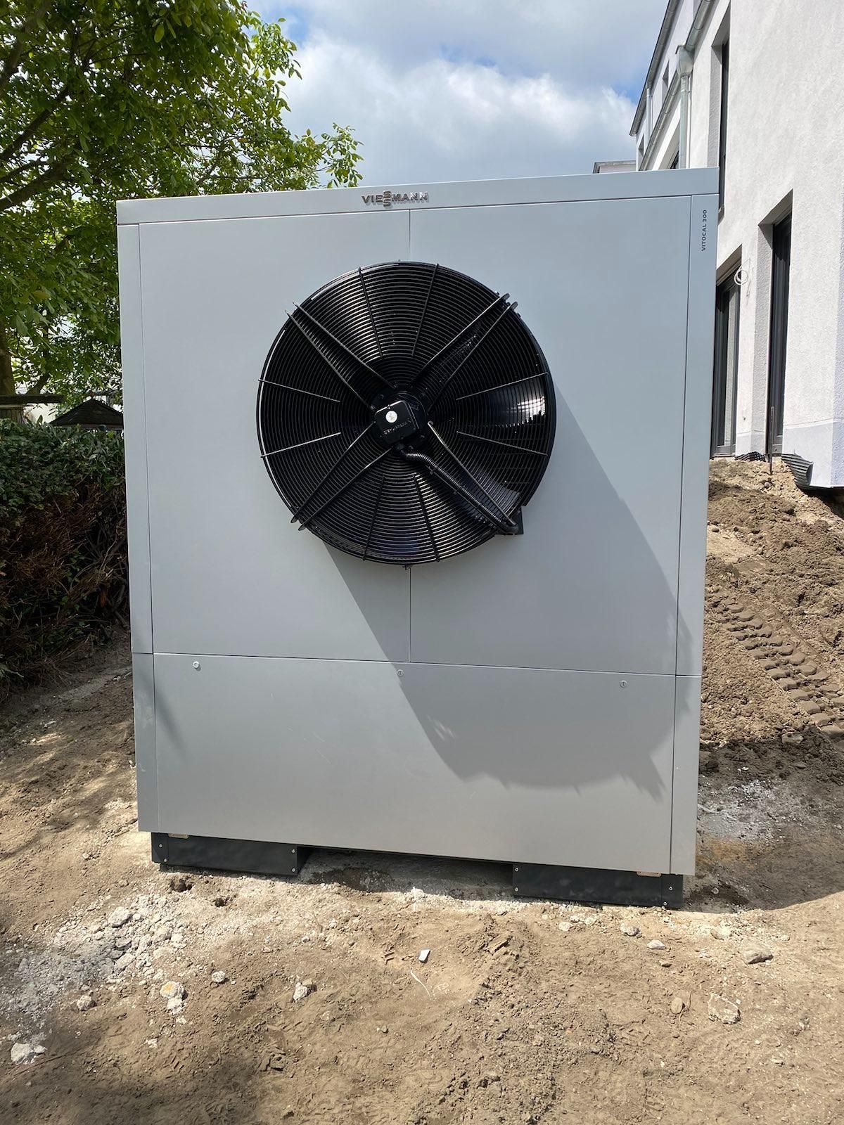 Große graue Industrieanlage mit einem schwarzen Ventilator an der Vorderseite, im Freien neben einem Gebäude.