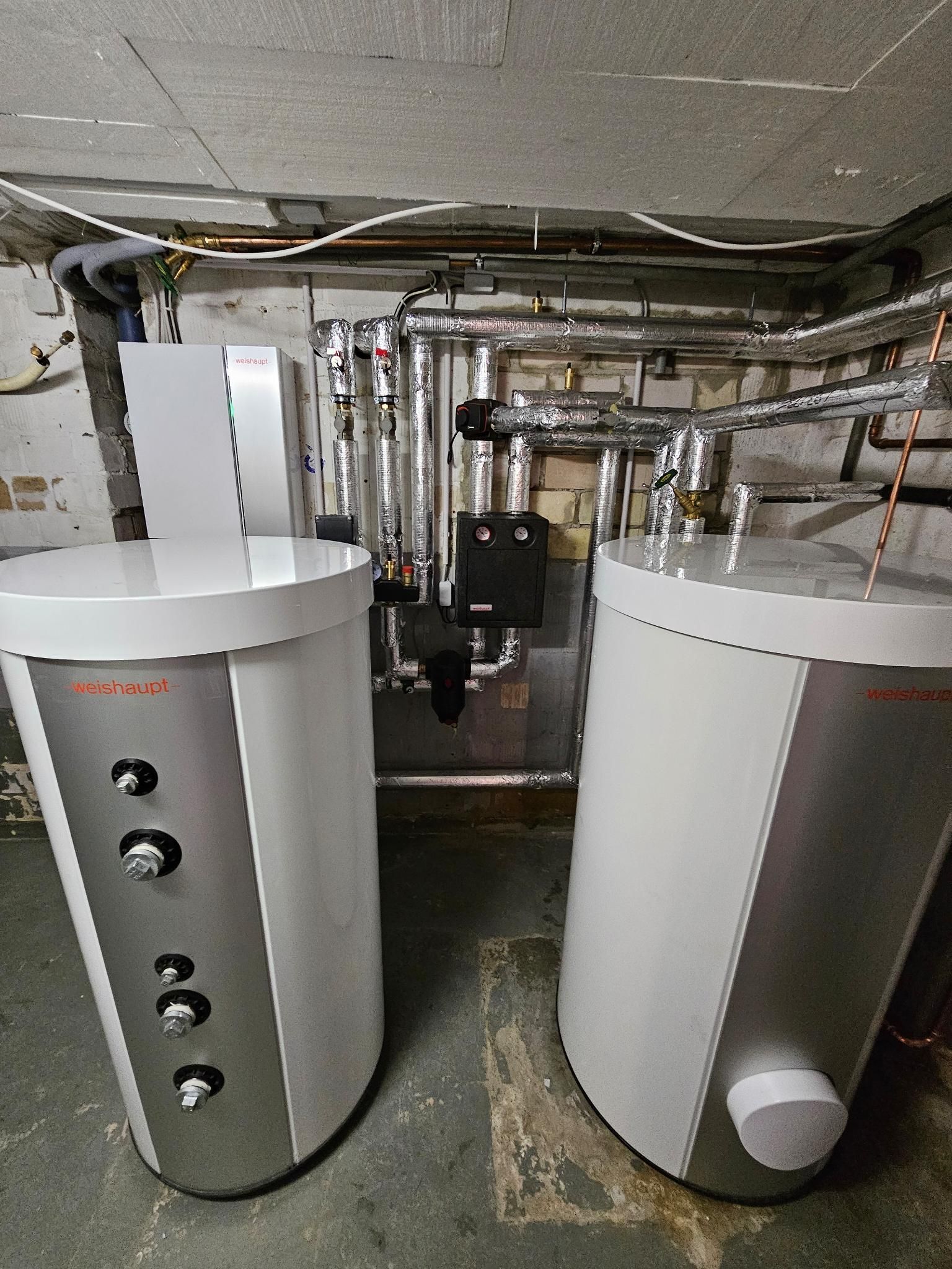 Zwei weiße, zylindrische Warmwasserbereiter in einem Keller-Hauswirtschaftsraum mit freiliegenden Rohren