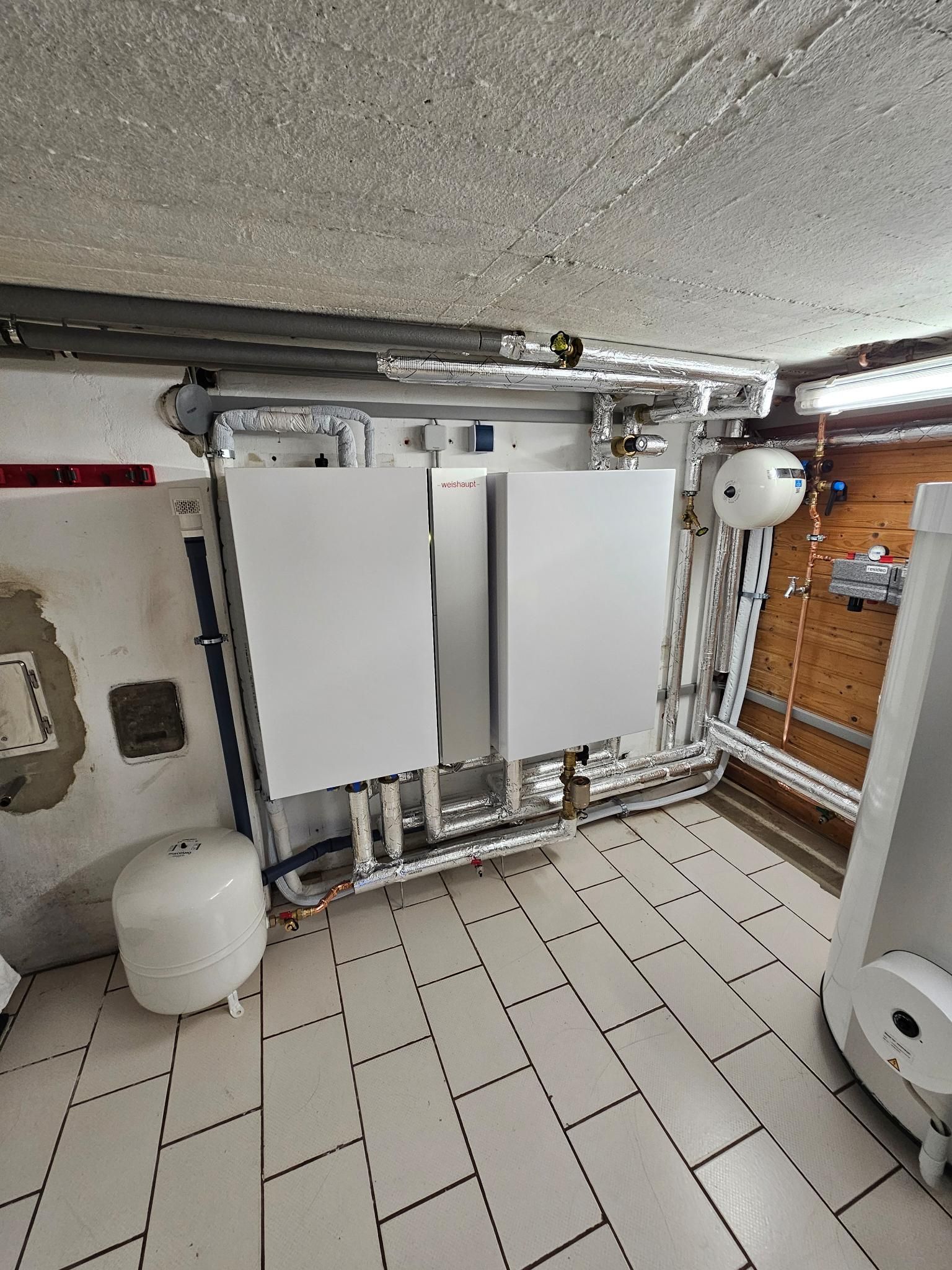 Hauswirtschaftsraum im Keller mit wandmontierten Klimaanlagen, freiliegenden Rohrleitungen und gefliestem Boden.